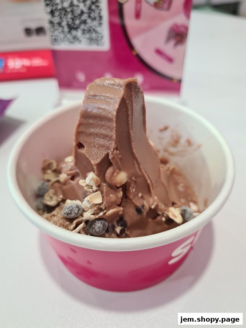 A cup of chocolate frozen yogurt topped with nuts and chocolate chips.
