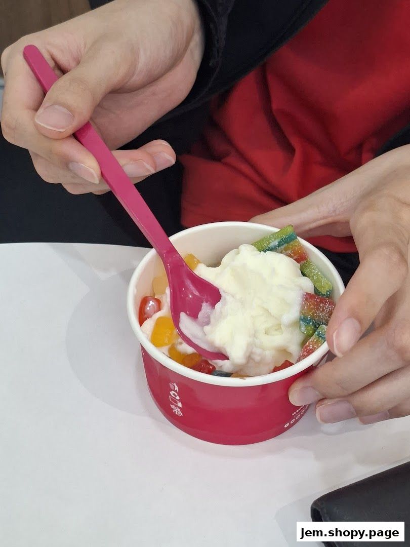 A person is eating frozen yogurt with colorful candy toppings using a pink spoon.