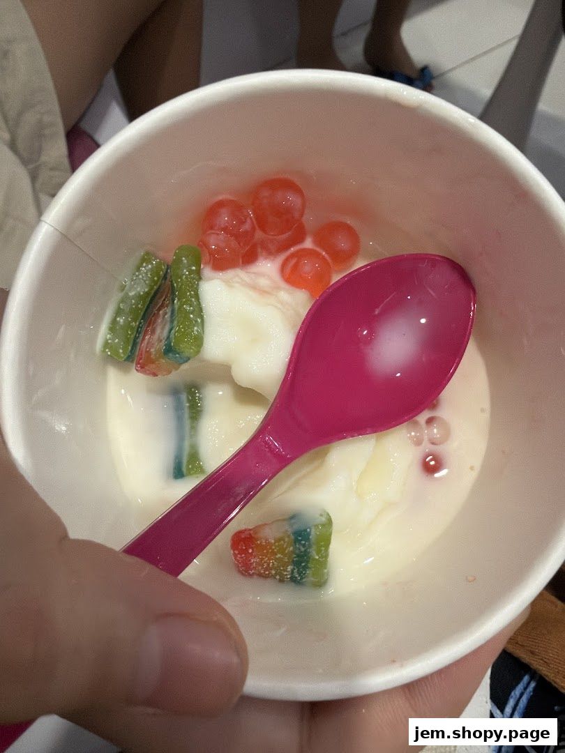 A cup of frozen yogurt with colorful candy toppings and a pink spoon.