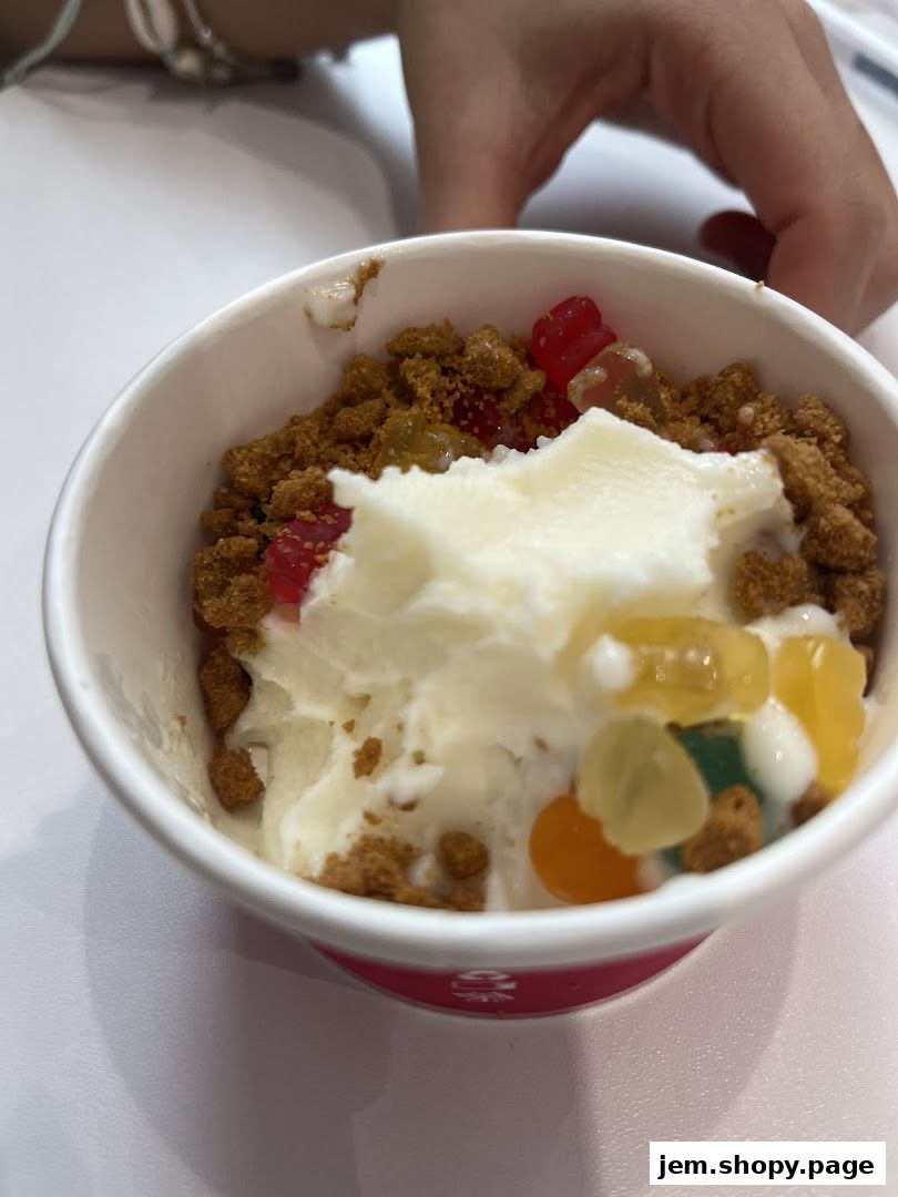 A cup of frozen yogurt topped with cookie crumbles and gummy bears.