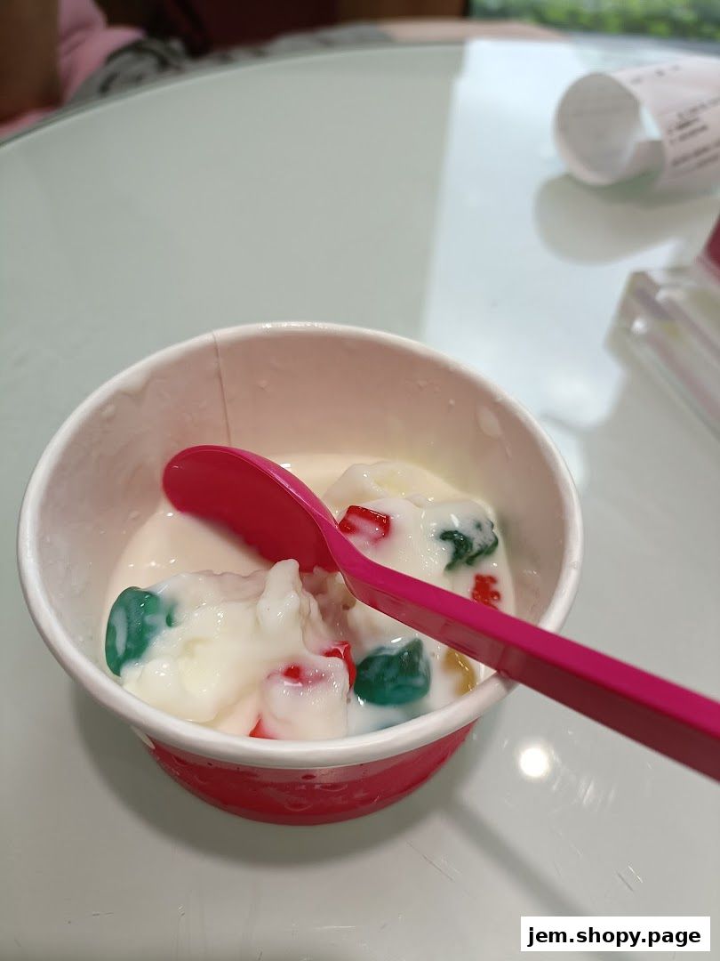 A cup of frozen yogurt with colorful toppings and a pink spoon.