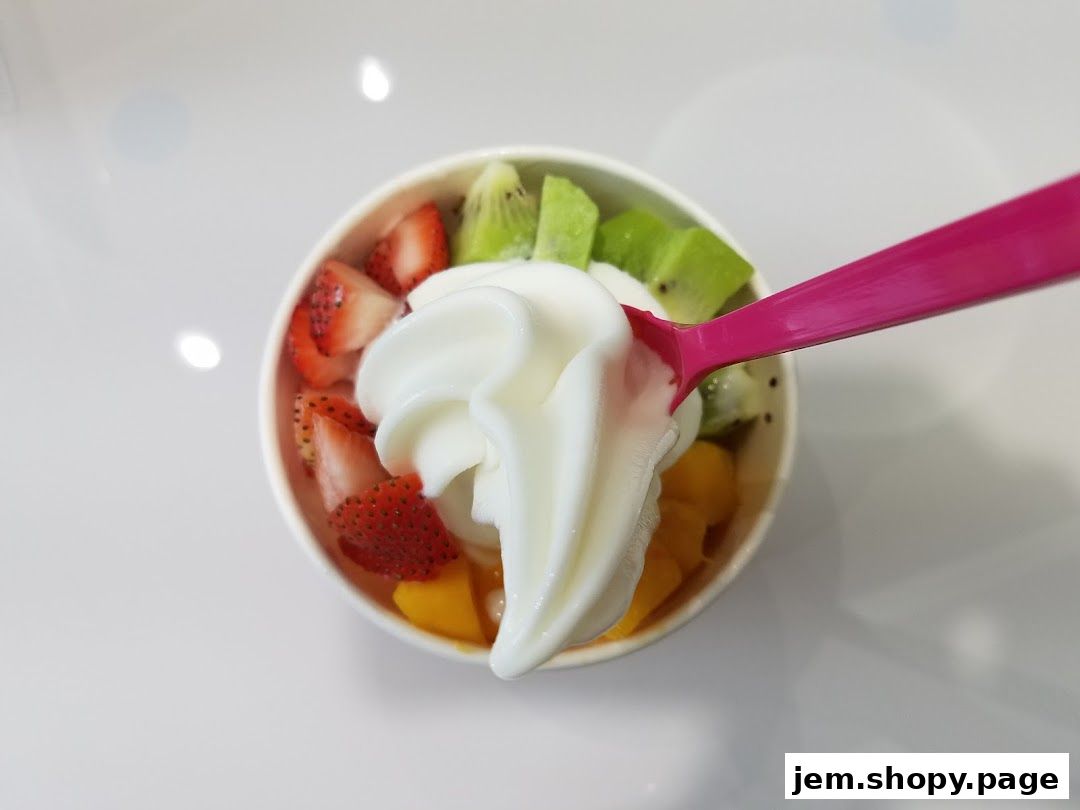 A cup of frozen yogurt topped with fresh strawberries, kiwi, and mango, with a pink spoon.