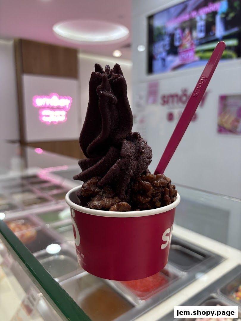 A cup of dark purple frozen yogurt topped with nuts and a pink spoon.