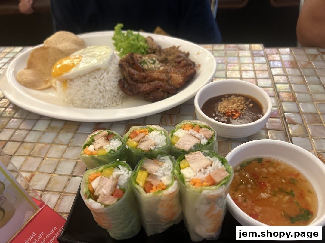 A plate of Vietnamese food featuring rice, a fried egg, spring rolls, and dipping sauces.