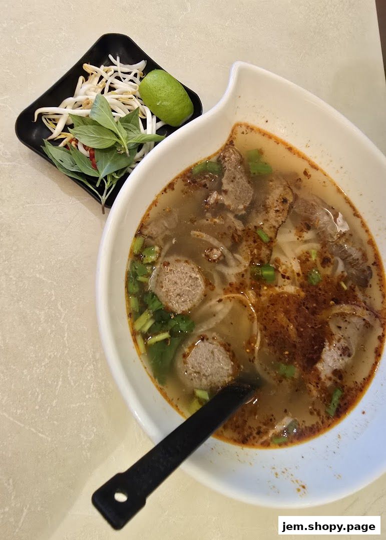 A steaming bowl of pho with beef and meatballs, served with bean sprouts, basil, and lime.