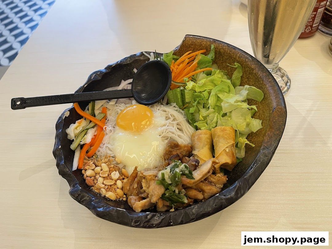A bowl of Vietnamese noodle salad with chicken, egg, spring rolls, and vegetables.