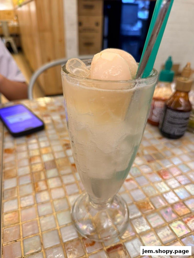 A refreshing lychee drink with ice and fruit, served in a tall glass with a straw.