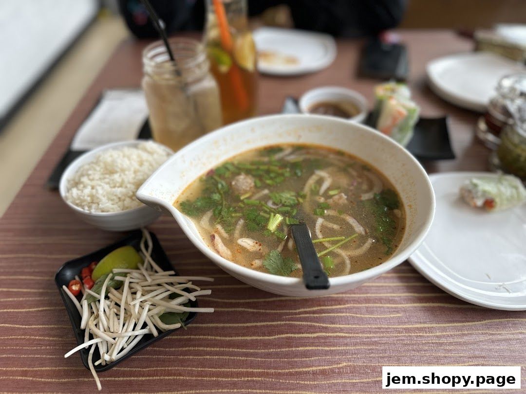 A bowl of pho with rice, spring rolls, and drinks on a table.