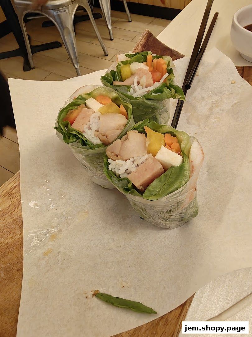 Three fresh spring rolls filled with vegetables and meat, served on parchment paper.