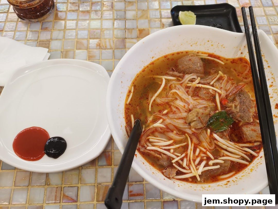 A steaming bowl of pho with beef and noodles, served with dipping sauces.