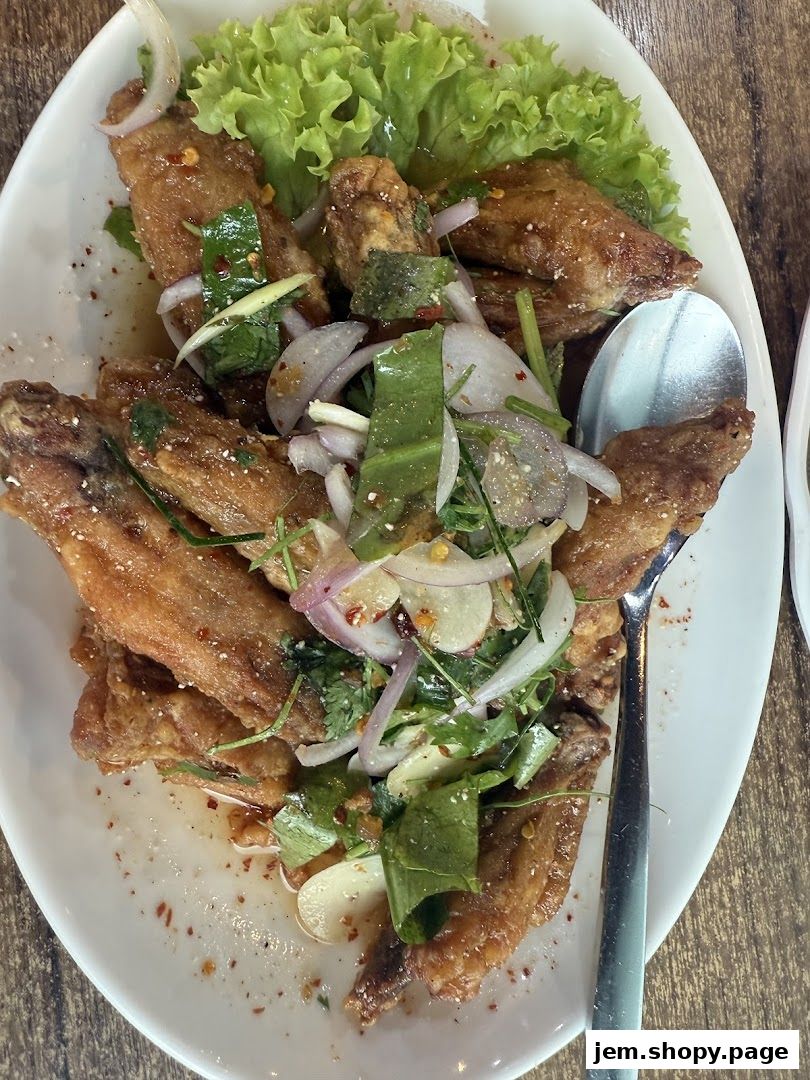 A plate of crispy Thai chicken wings topped with fresh herbs, onions, and chili flakes.