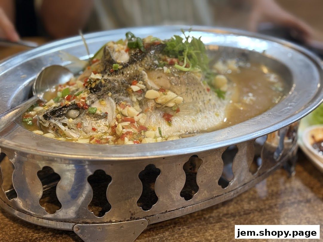 A close-up of a whole steamed fish dish with chili, garlic, and herbs.