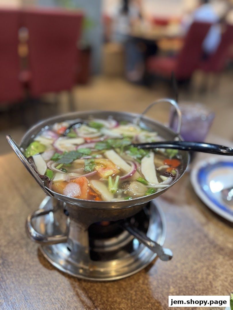 A steaming pot of Thai soup with vegetables and herbs sits on a burner.