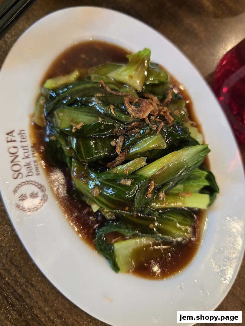 A plate of stir-fried green vegetables with sauce and crispy fried shallots.