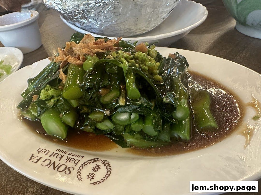 A plate of stir-fried green vegetables with sauce and crispy fried shallots.