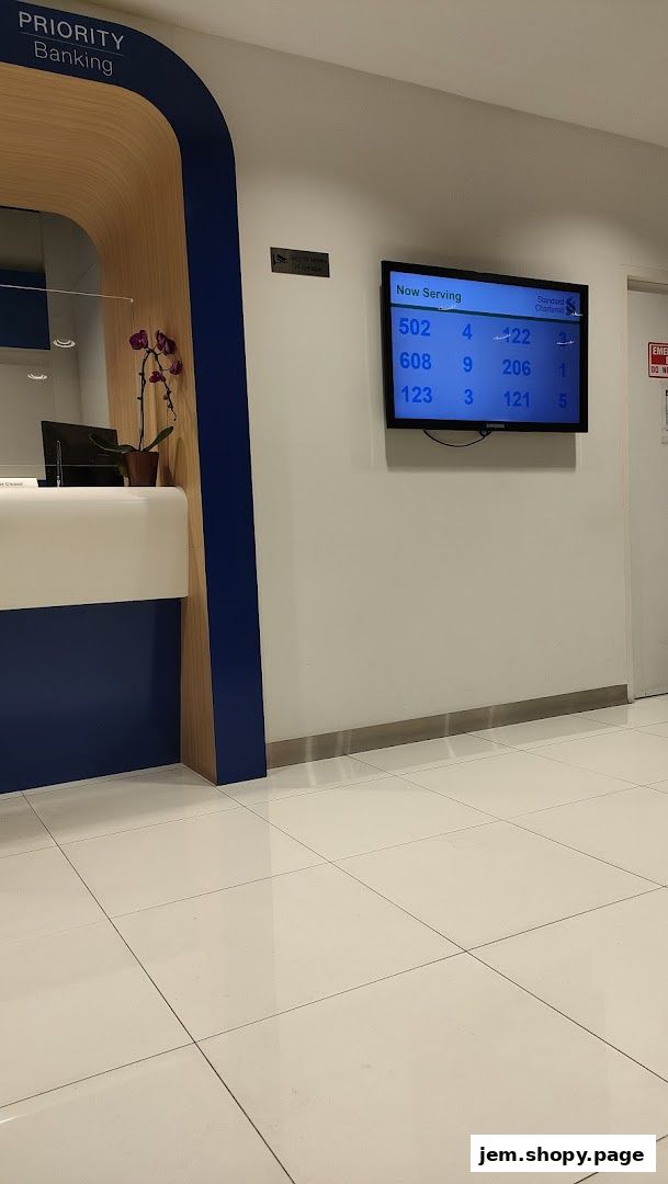 Interior of a Standard Chartered Bank with a 'Now Serving' display and 'Priority Banking' signage.