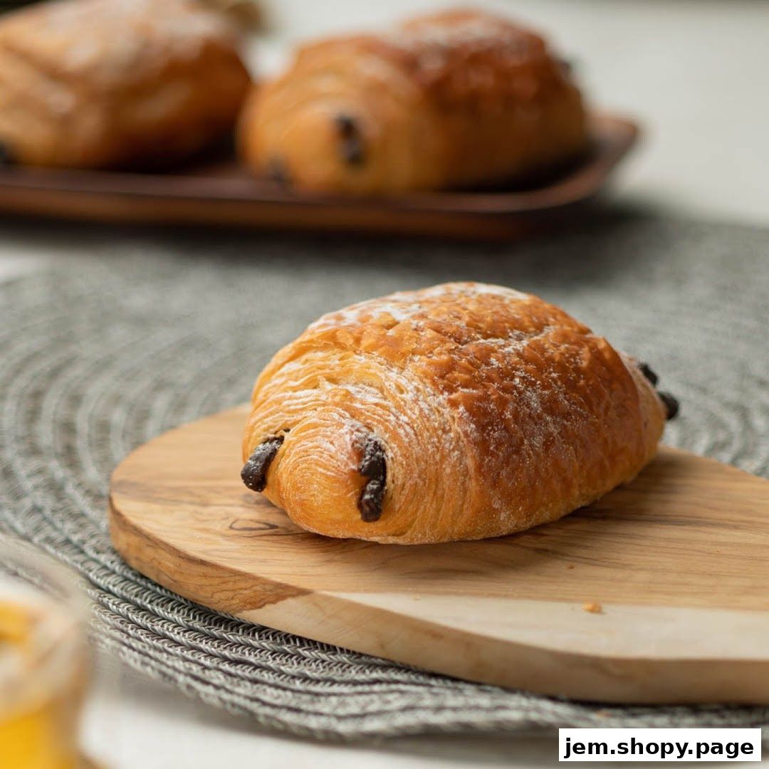 A close-up of a chocolate croissant dusted with powdered sugar on a wooden board.