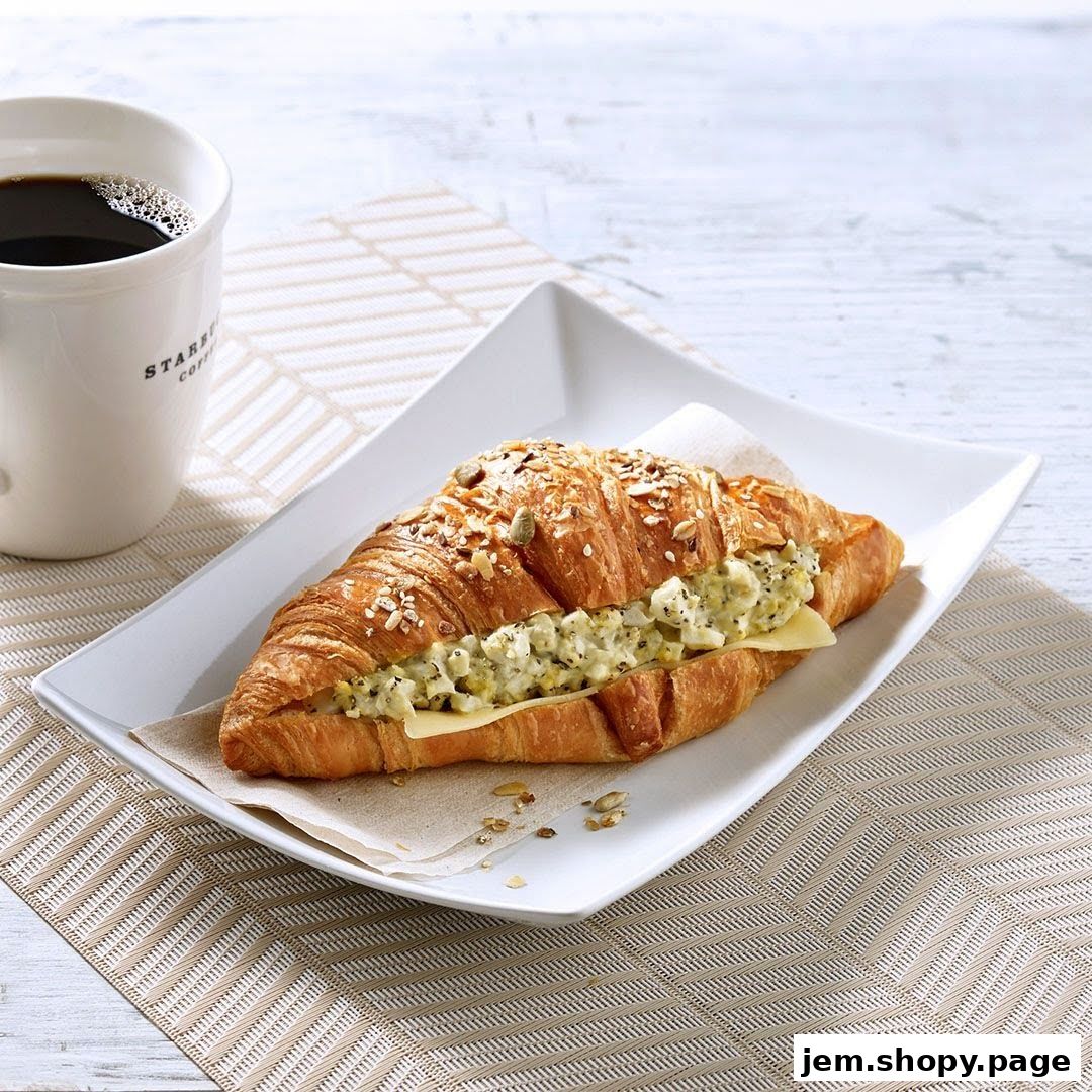 A croissant sandwich filled with egg salad and cheese, served with a cup of coffee.