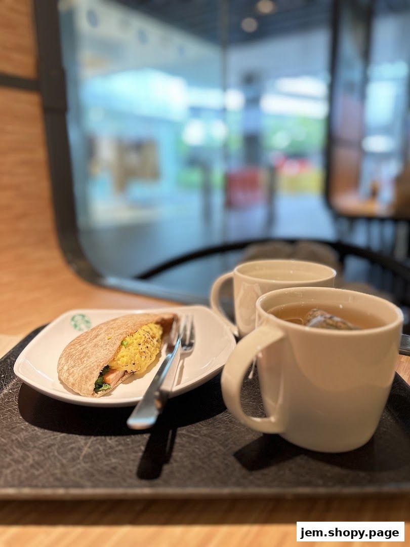 A breakfast meal with a pita sandwich and two cups of tea on a tray.