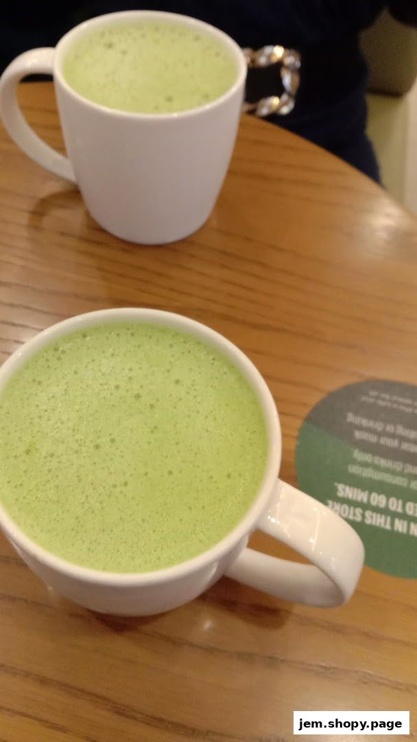 Two cups of frothy green matcha tea on a wooden table.