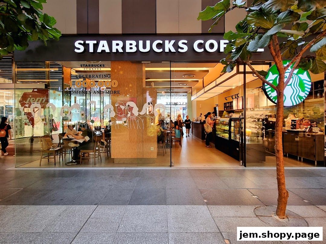 Exterior view of a Starbucks coffee shop with people inside and a tree in the foreground.