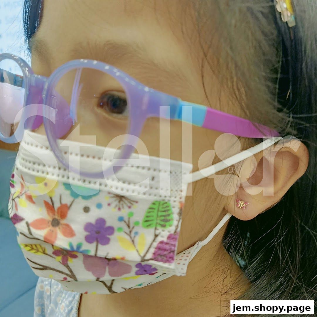 Close-up of a child wearing glasses and a floral mask, showing a butterfly earring.