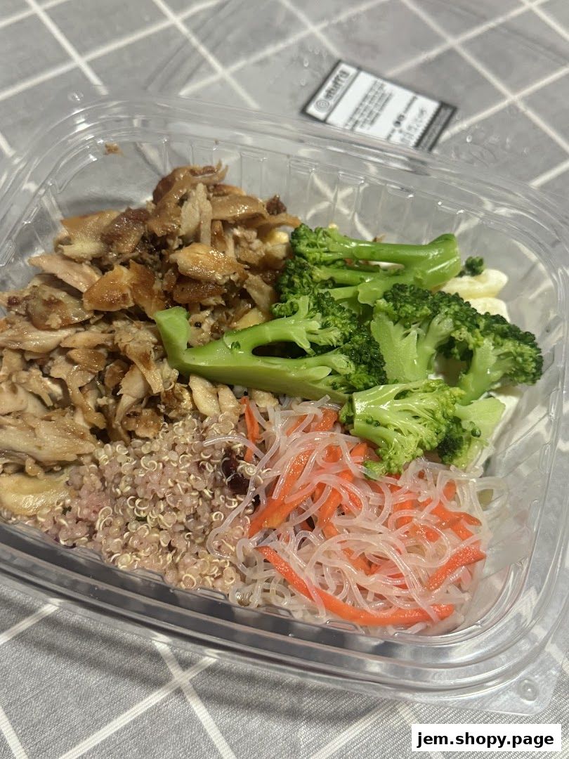 A clear plastic container filled with a healthy meal of chicken, quinoa, broccoli, and noodles.