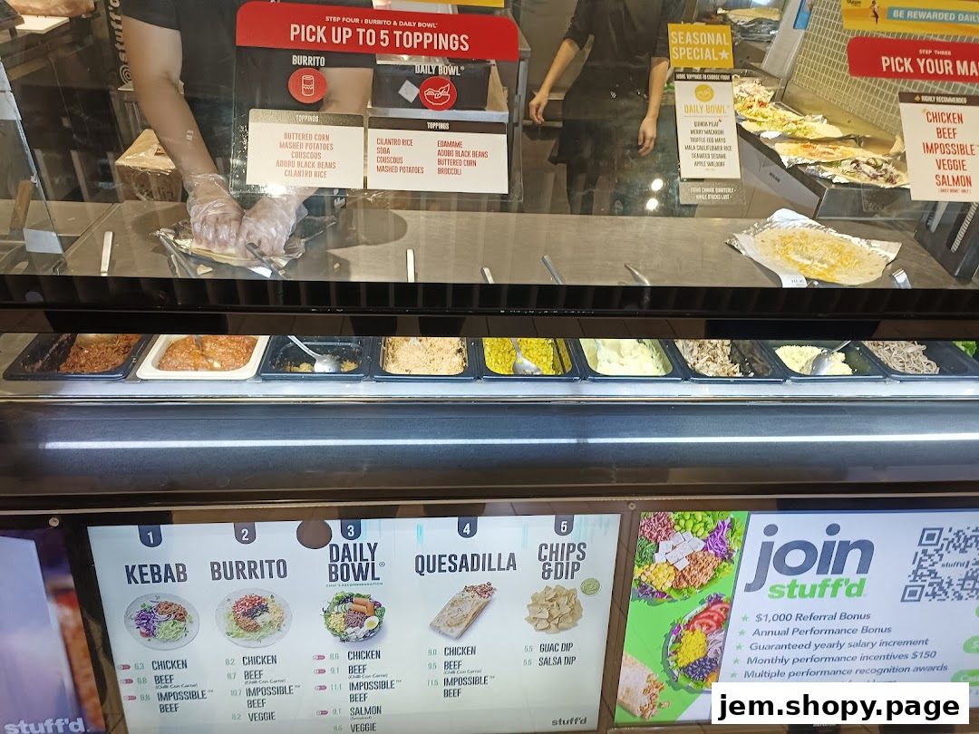A food counter with various toppings and a digital menu displaying meal options and employment opportunities.