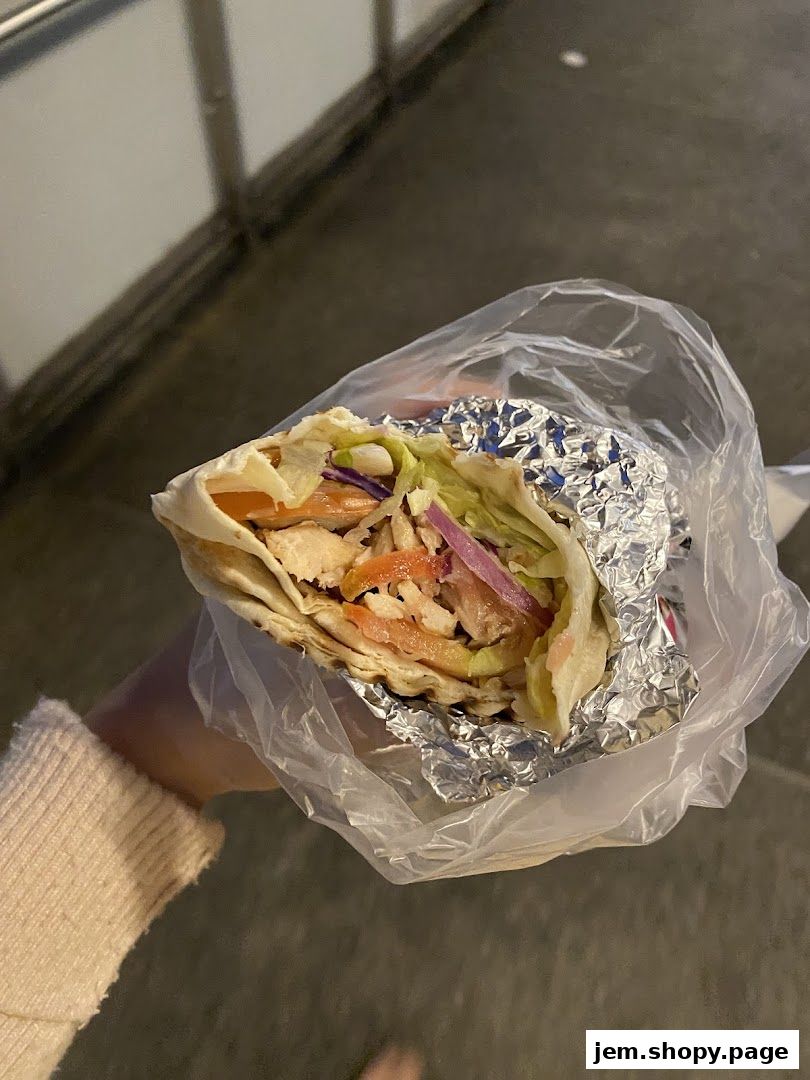 A hand holds a freshly made wrap filled with meat, vegetables, and sauce.