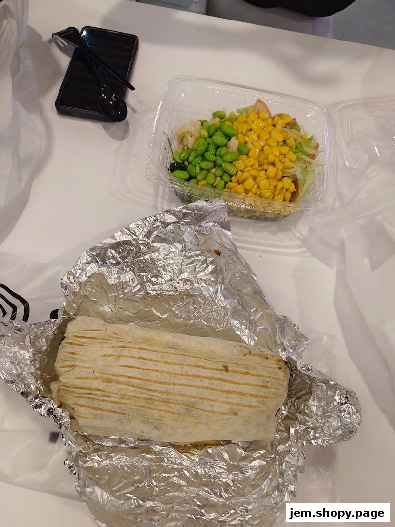 A foil-wrapped burrito and a salad in a plastic container on a white table.