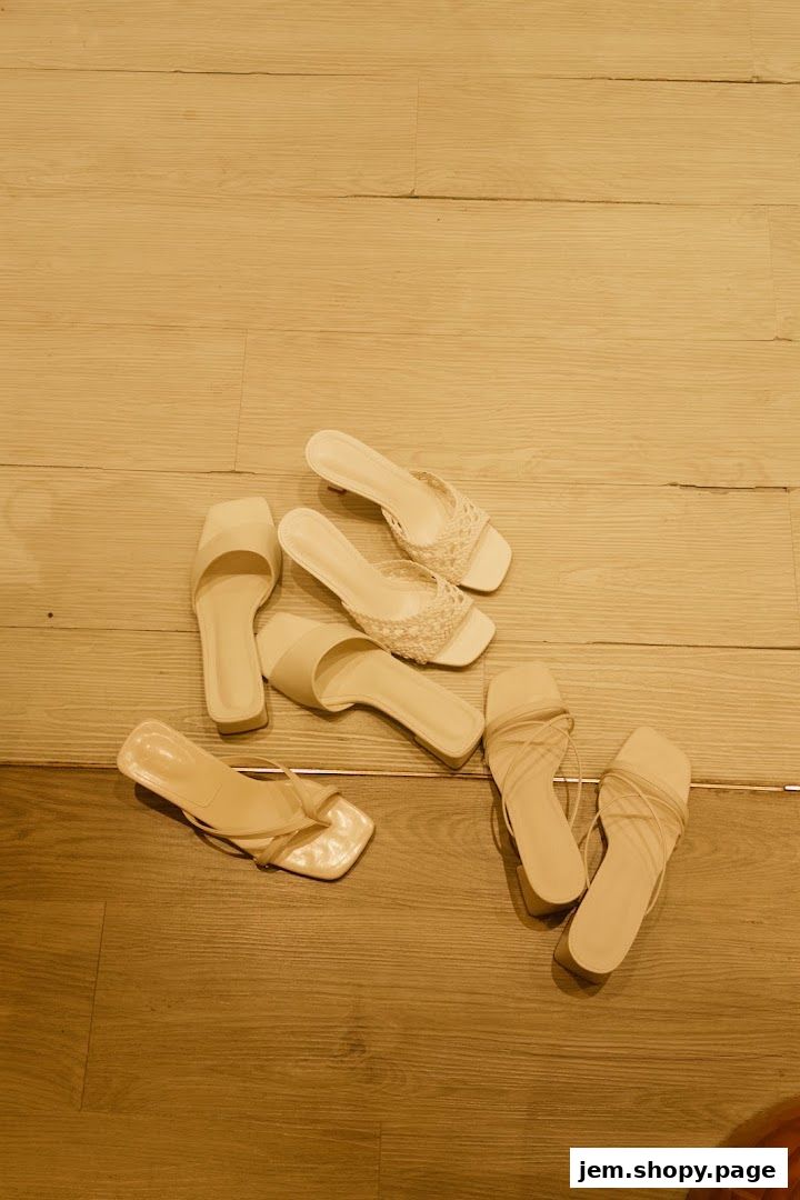 A collection of stylish, neutral-colored women's sandals laid out on a wooden floor.