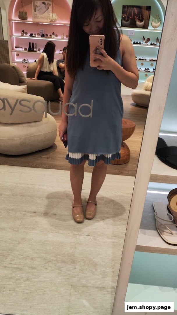 A woman takes a mirror selfie in a shoe store, showcasing her outfit and the store's interior.