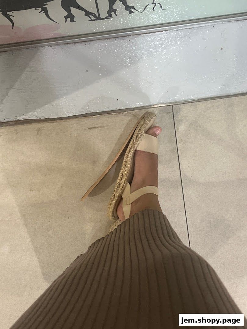 A person wearing beige sandals and a ribbed brown skirt stands on a tiled floor.