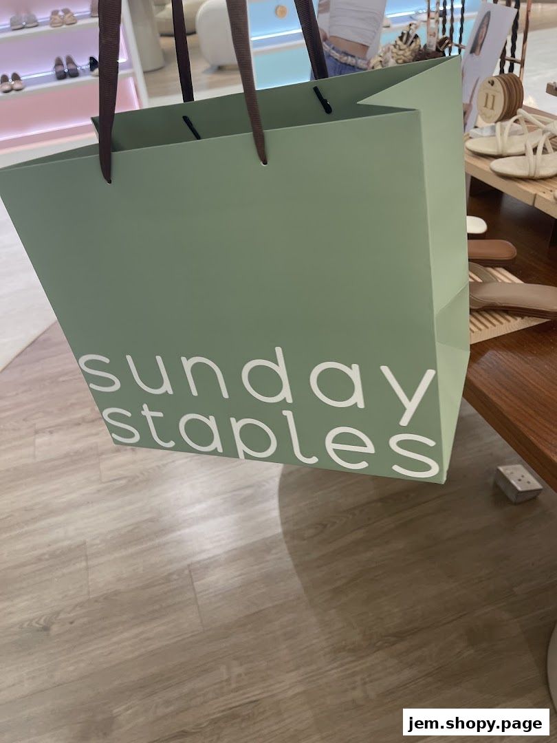 A green shopping bag with 'sunday staples' logo in white, inside a store.