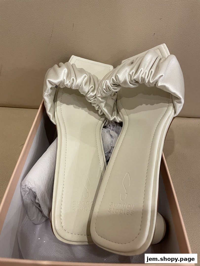 A pair of cream-colored ruched sandals from Sunday Staples in a box.