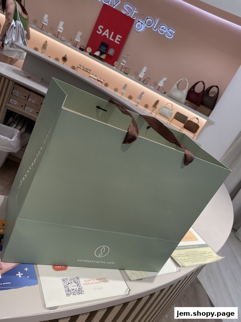 A shopping bag from Sunday Staples with a sale sign and display of bags in the background.