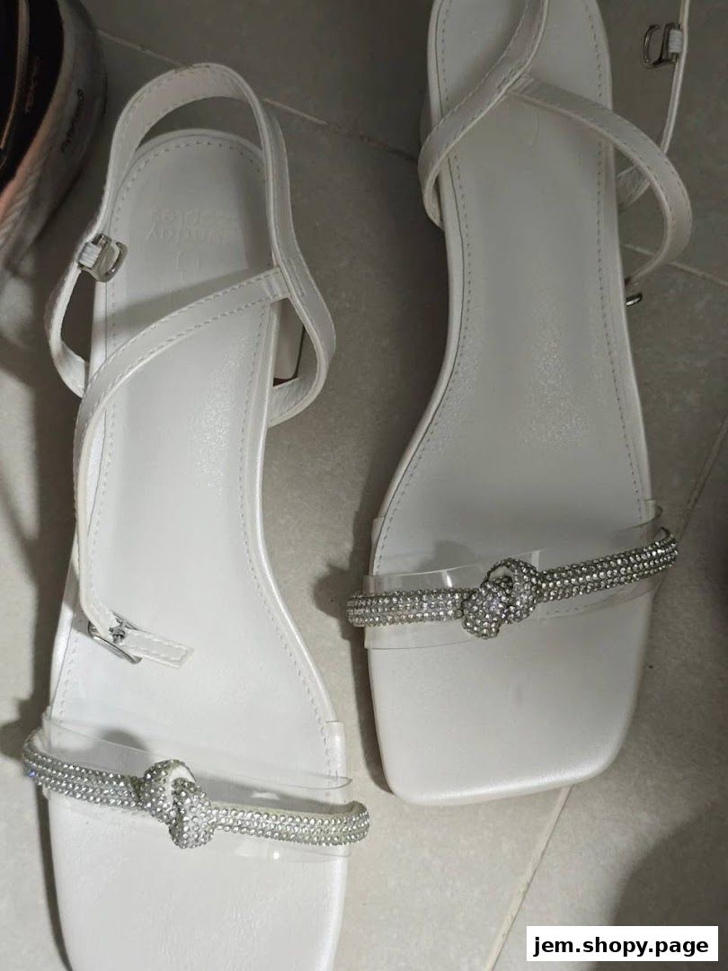 A pair of white sandals with clear straps and rhinestone embellishments.