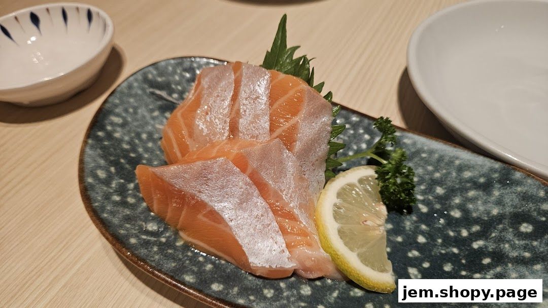 Fresh salmon sashimi served on a decorative plate with lemon and parsley.