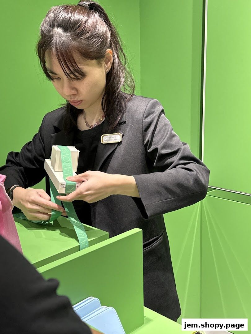 A sales associate is carefully wrapping a gift with branded ribbon at a counter.