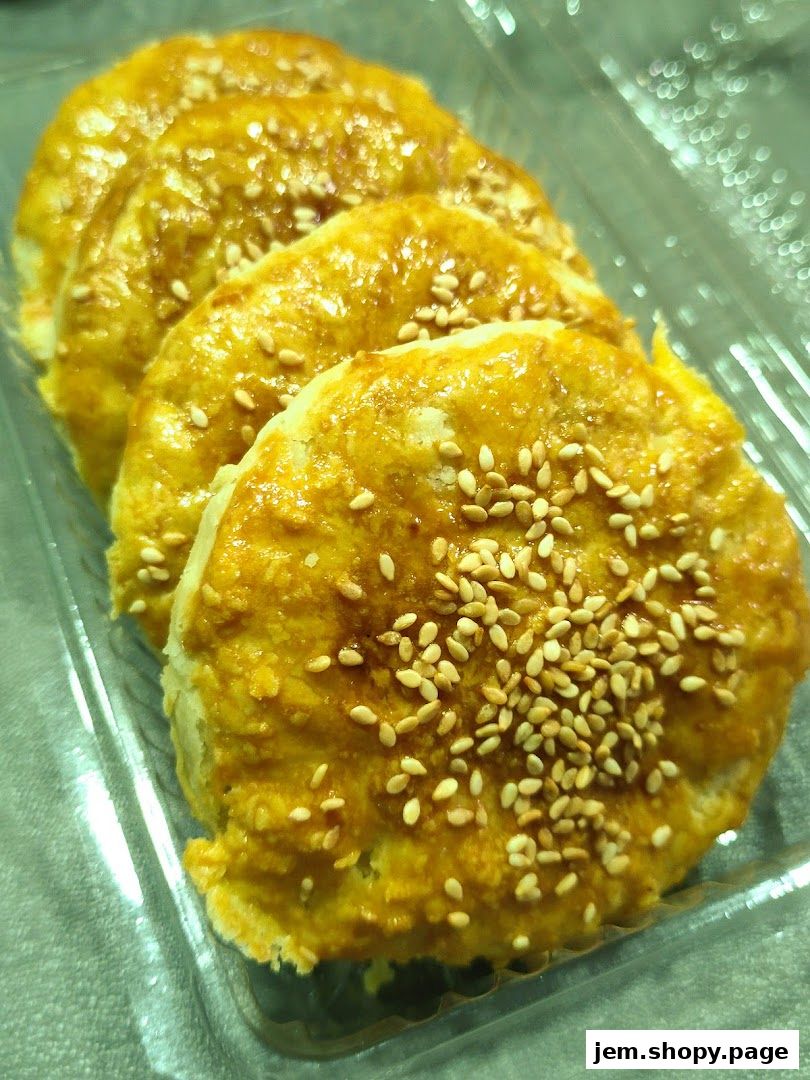 A close-up shot of golden-brown pastries topped with sesame seeds in a clear plastic container.