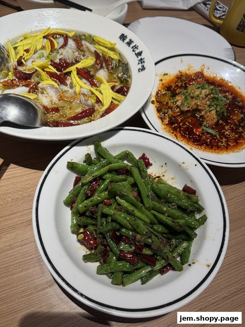 Three dishes of Chinese food, including fish, green beans, and a spicy appetizer, are served on a wooden table.