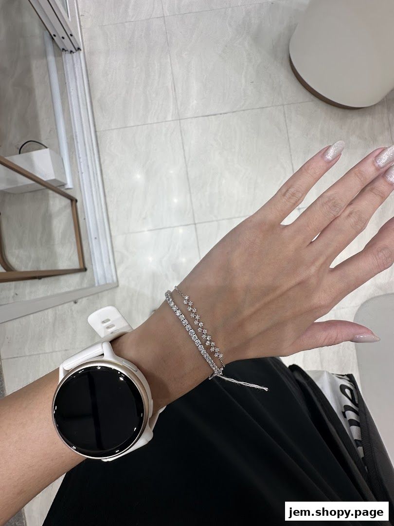 A person wearing a white smartwatch and two delicate diamond bracelets on their wrist.