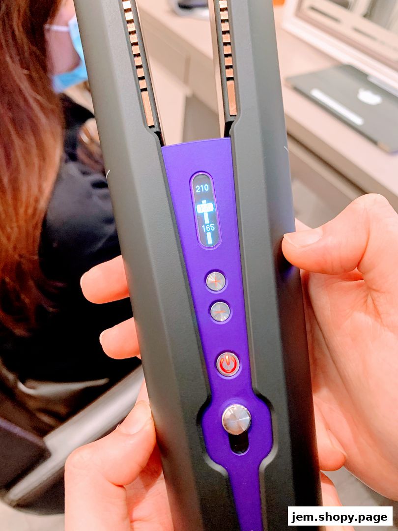 Close-up of a person holding a professional hair straightening iron with a digital display.