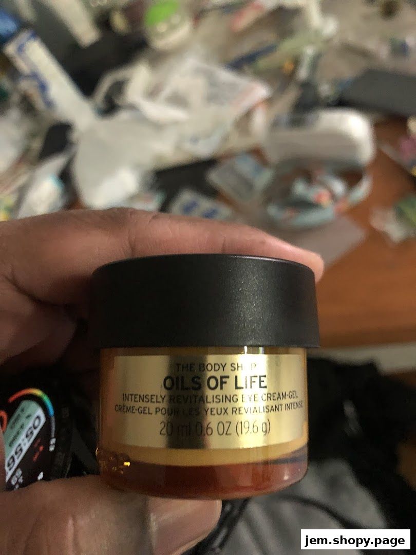 A hand holds a small jar of The Body Shop's Oils of Life eye cream.