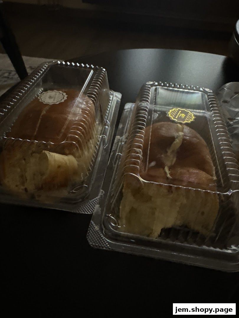 Two loaves of bread in clear plastic containers on a dark surface.