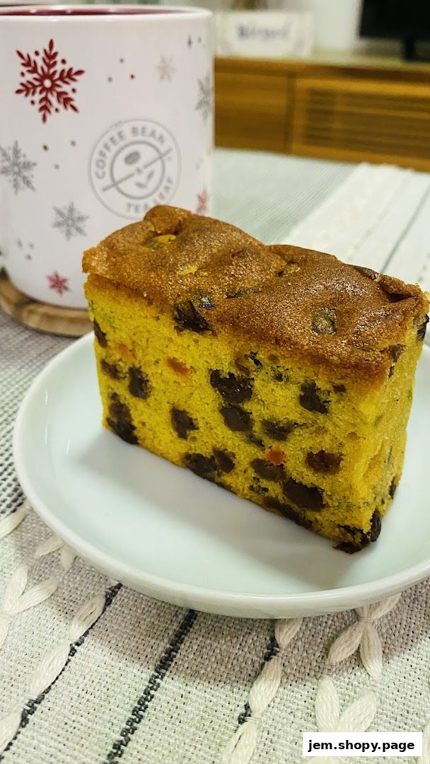 A slice of fruitcake on a white plate next to a festive mug.