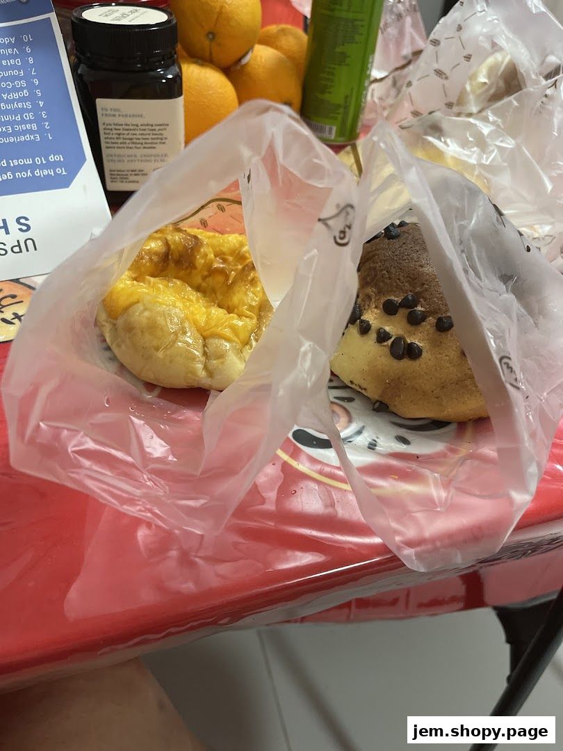 Two freshly baked bread items in plastic bags, with oranges and a bottle in the background.