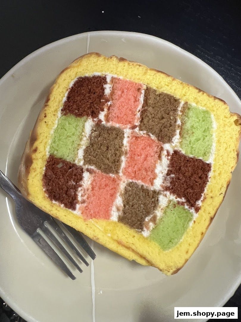 A slice of colorful checkerboard cake with cream filling on a plate with a fork.