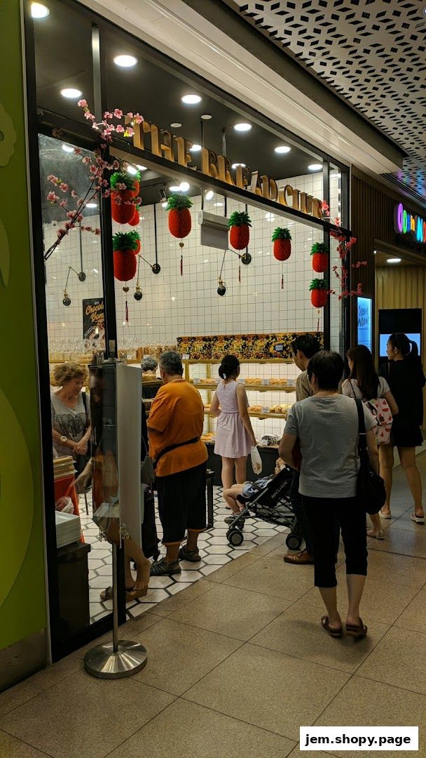 People are queuing outside a bakery called 'The Bread Club' with festive decorations.