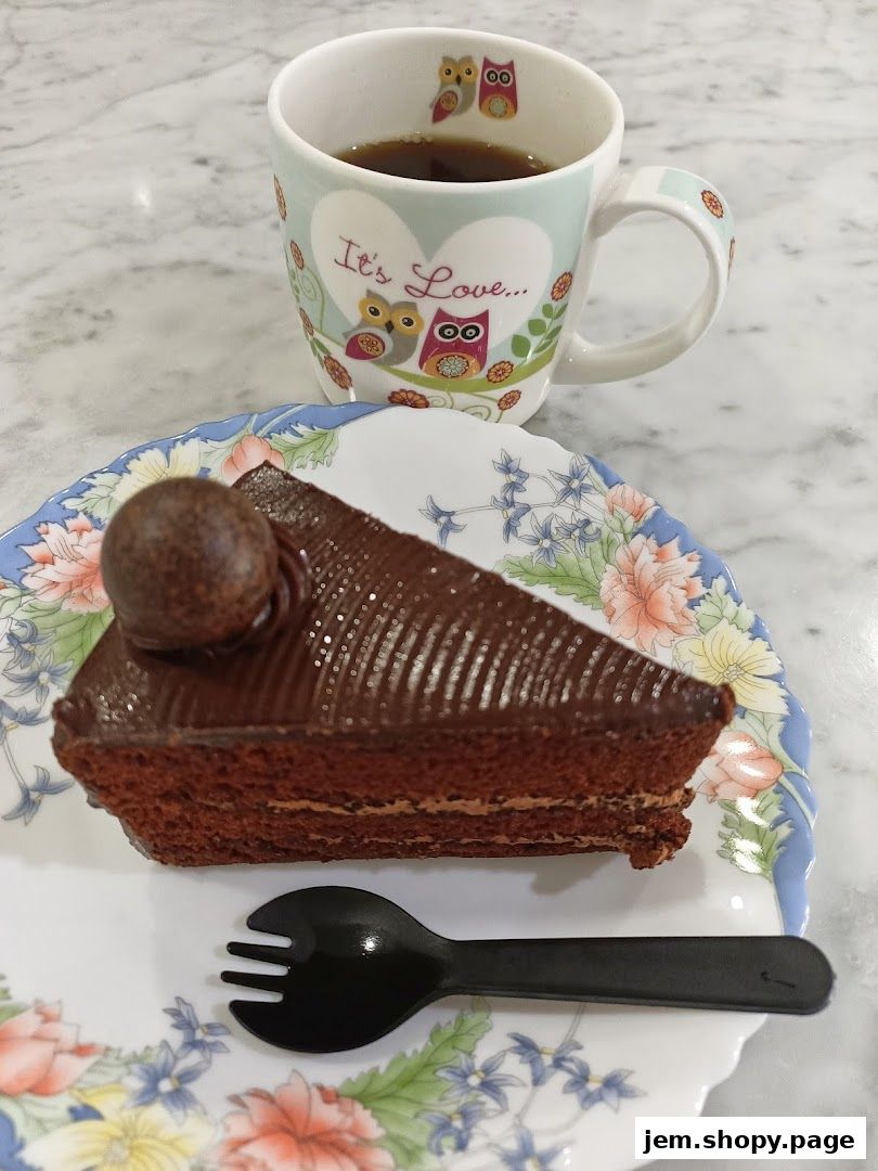 A slice of chocolate cake with a chocolate truffle and a cup of coffee.